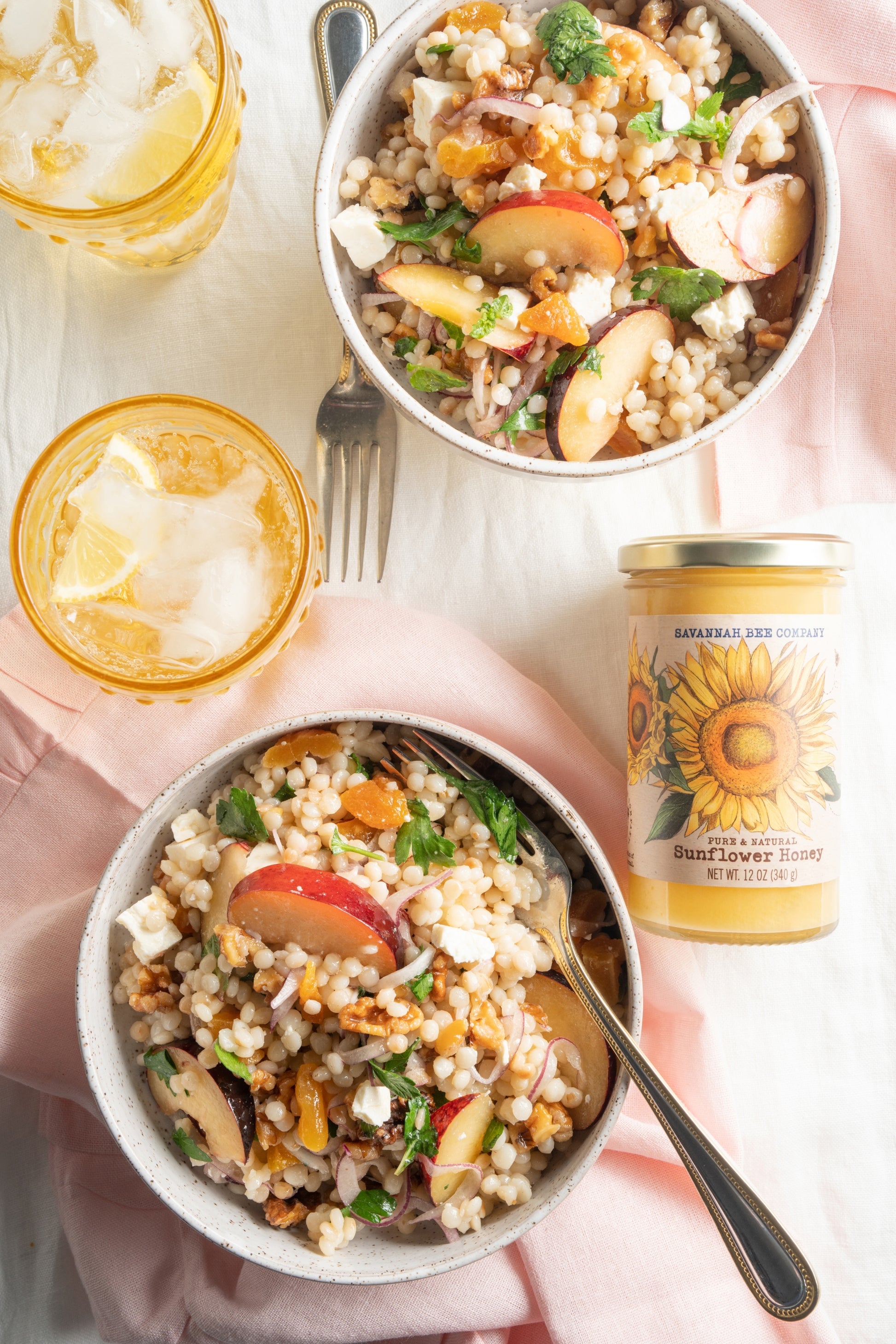 Two bowls of lemon herb cous cous salad made with sunflower honey dressing next to a 12 ounce jar of sunflower honey.