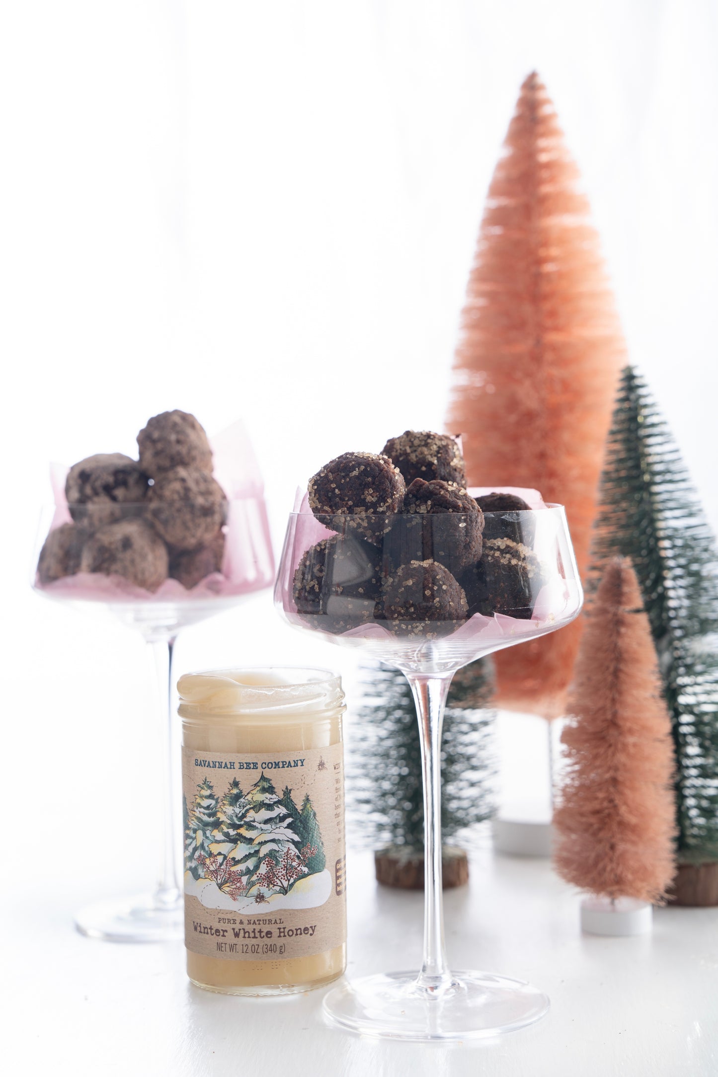 Two champagne glasses filled with brownie bourdon balls next to an open jar of winter white honey