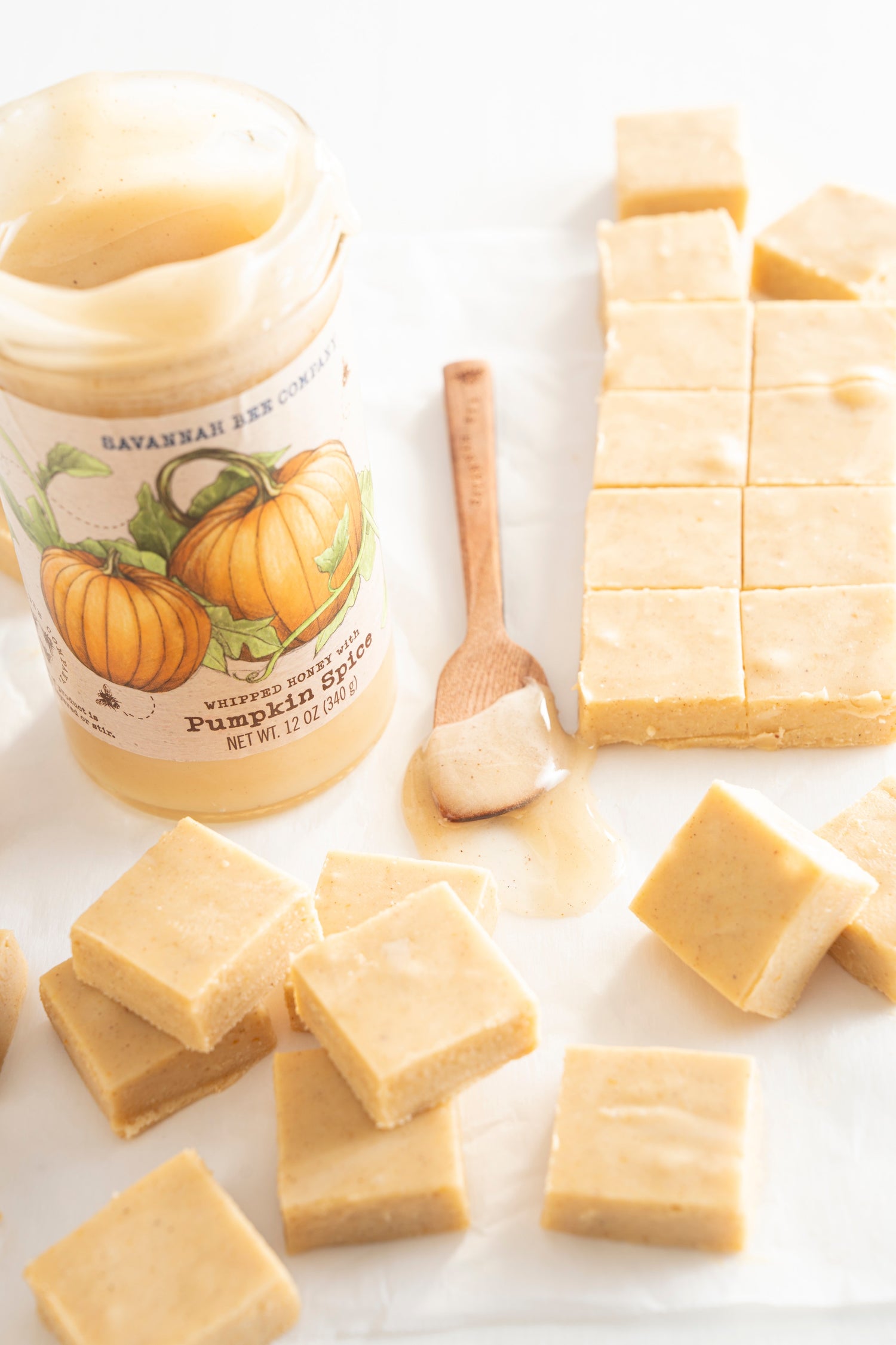 A block and a few squares of pumpkin spice whipped honey fudge next to a 12 ounce jar of pumpkin spice whipped honey