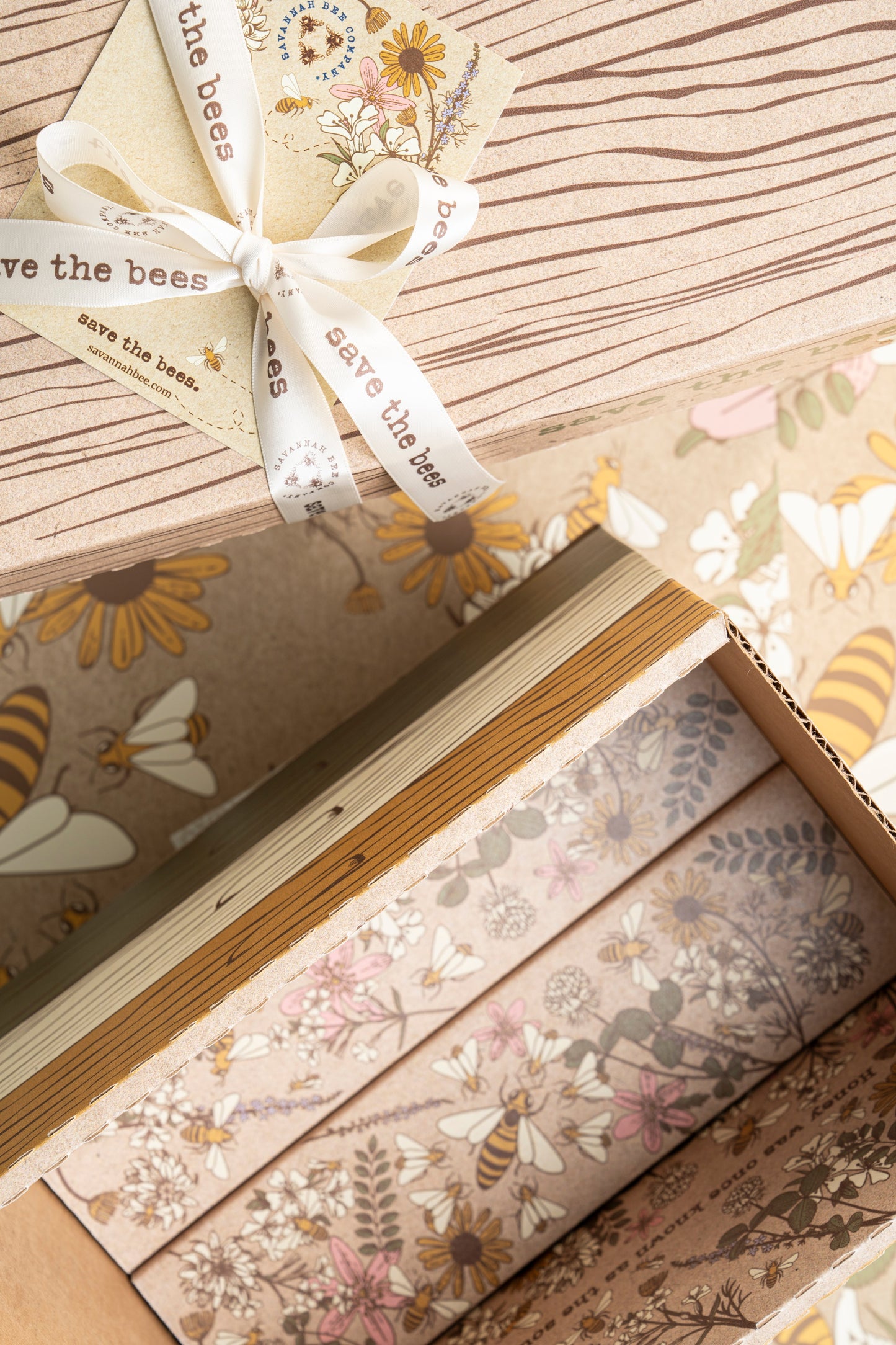 One opened gift box with floral pattern on the inside next to a closed gift box tied with a save the bees ribbon