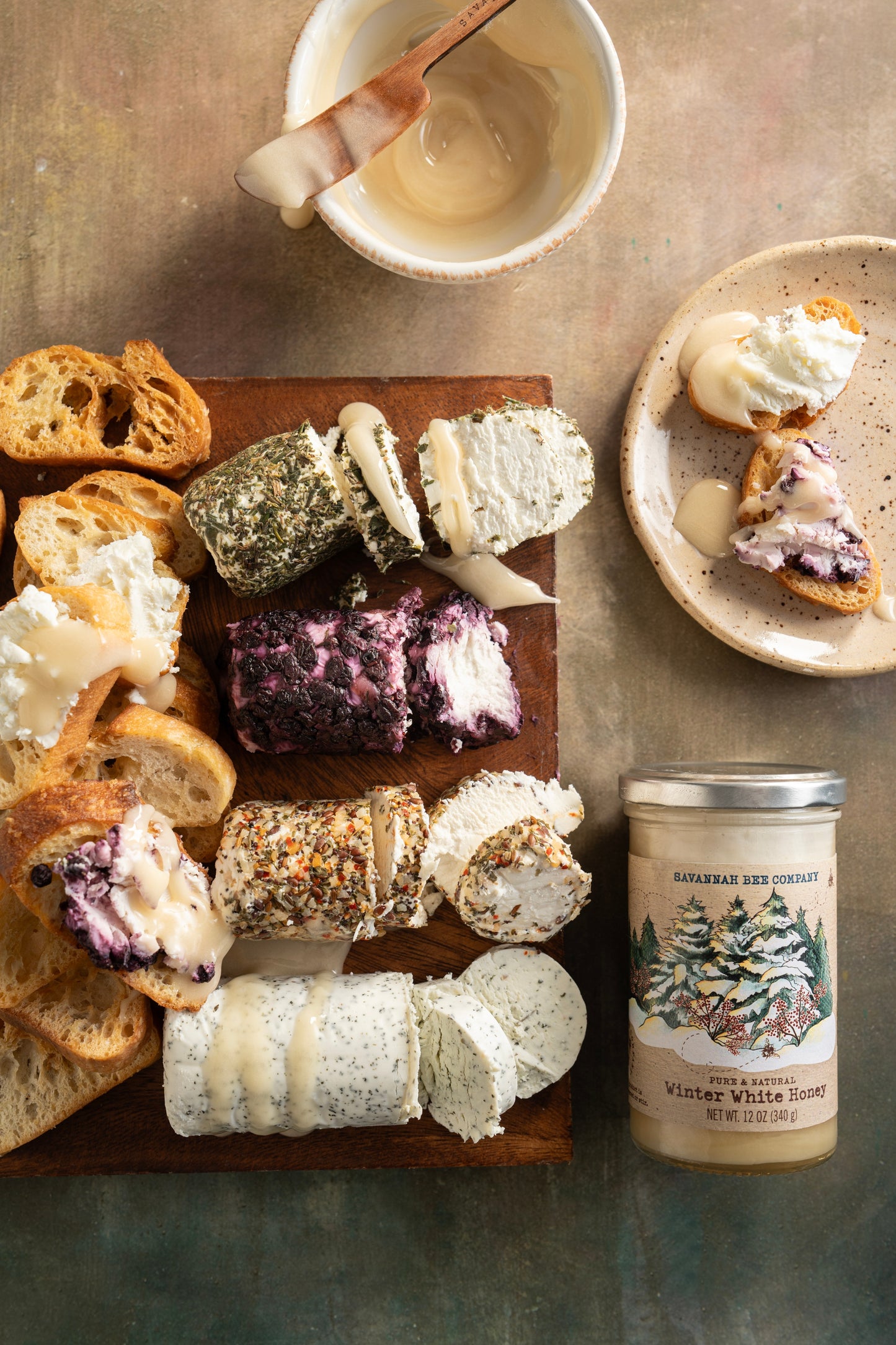 A tray with four different types of goat cheese, crostini, and a 12 ounce jar of winter white honey