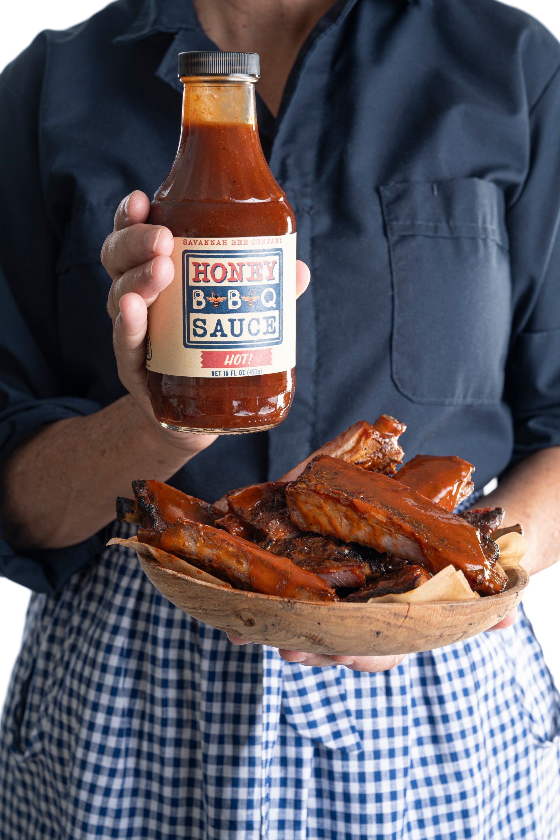 A model holding Savannah Bee Company hot BBQ sauce next to a bowl of ribs