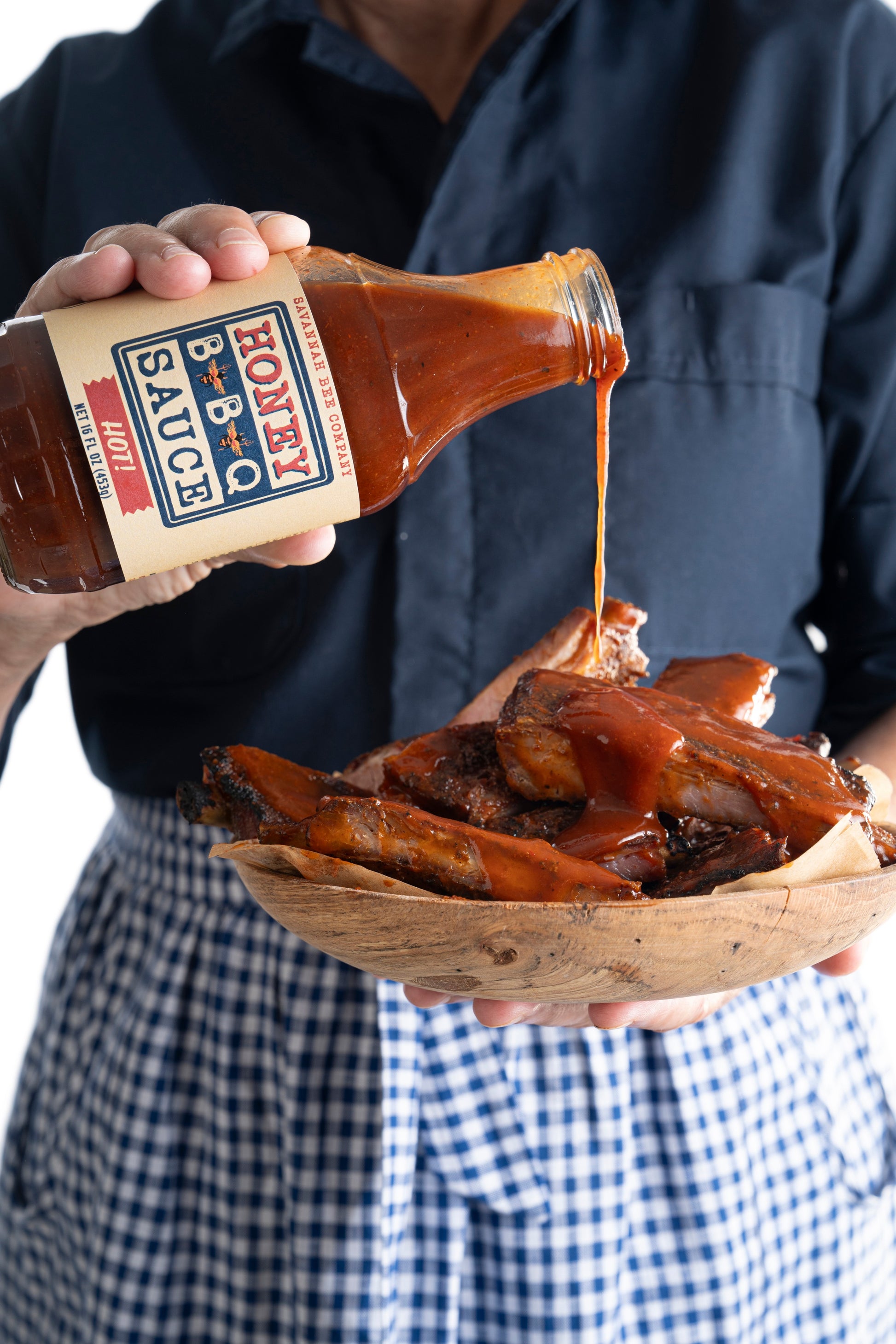 A model pouring Savannah Bee Company hot BBQ sauce on to a bowl of ribs