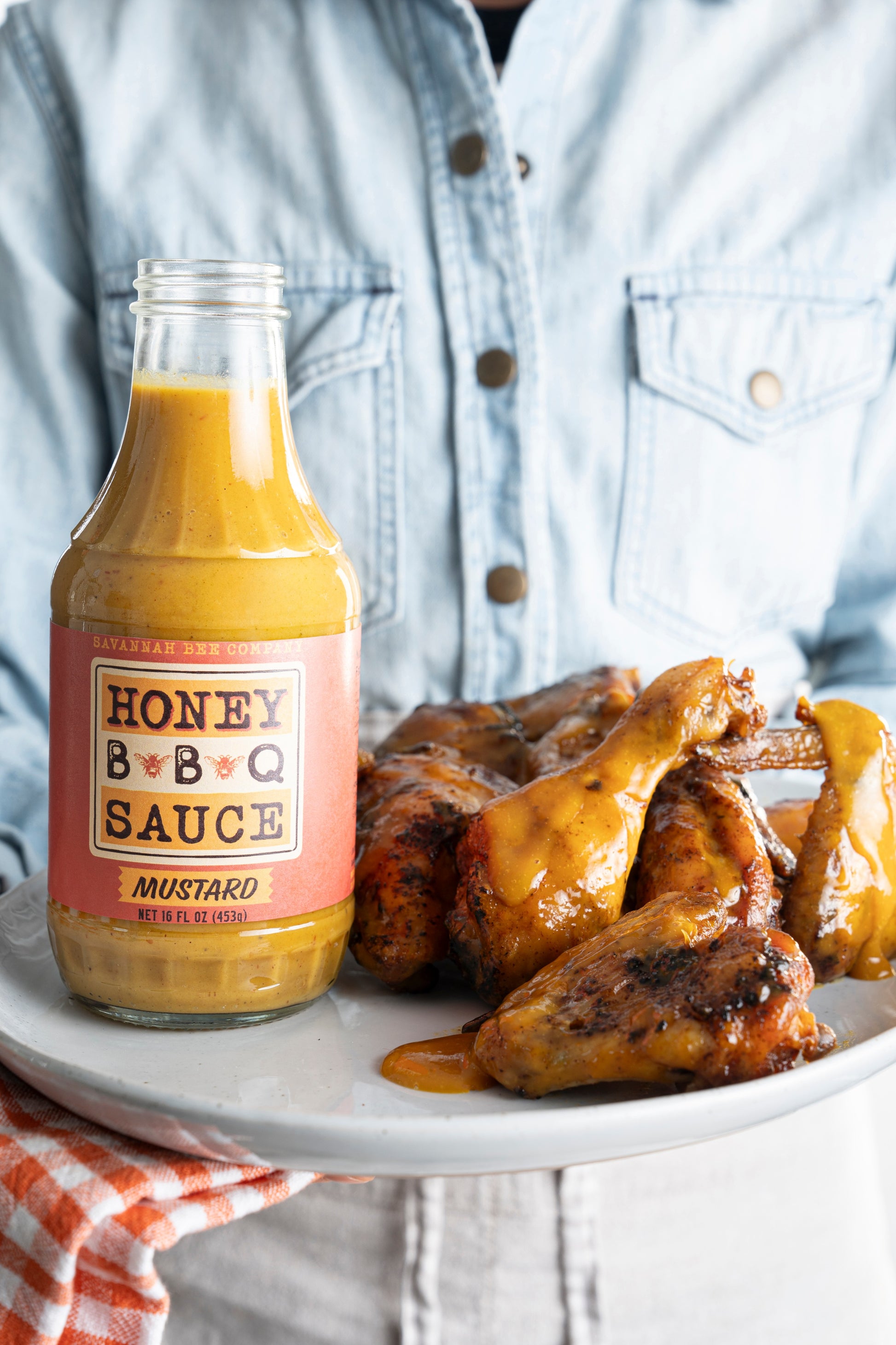 A model holding Savannah Bee Company mustard BBQ sauce bottle on a plate of chicken wings