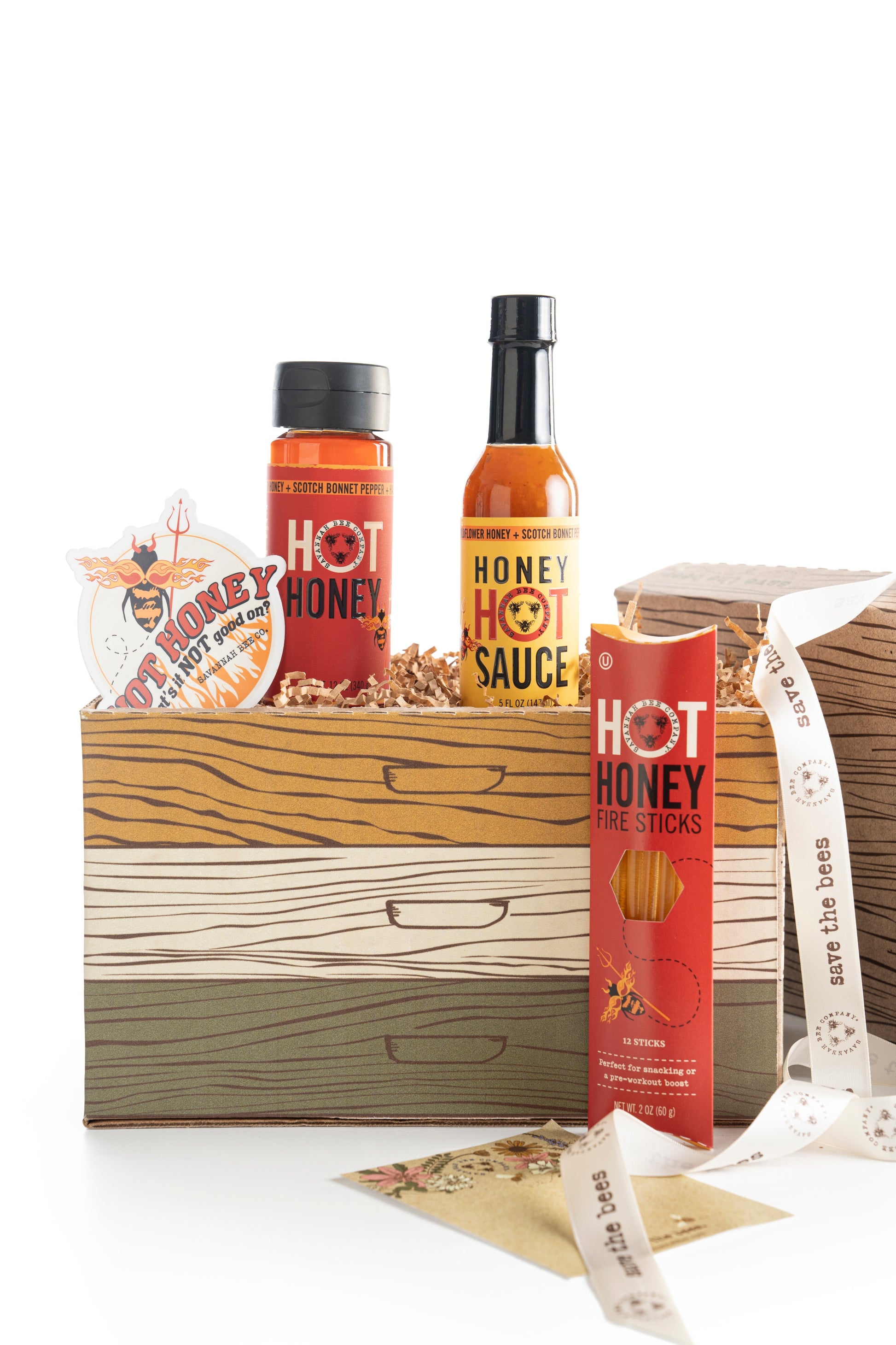 Gift box with Savannah Bee Company honey hot sauce, hot honey fire sticks, Hot Honey, and a hot honey sticker with a devil drone and flames, side view