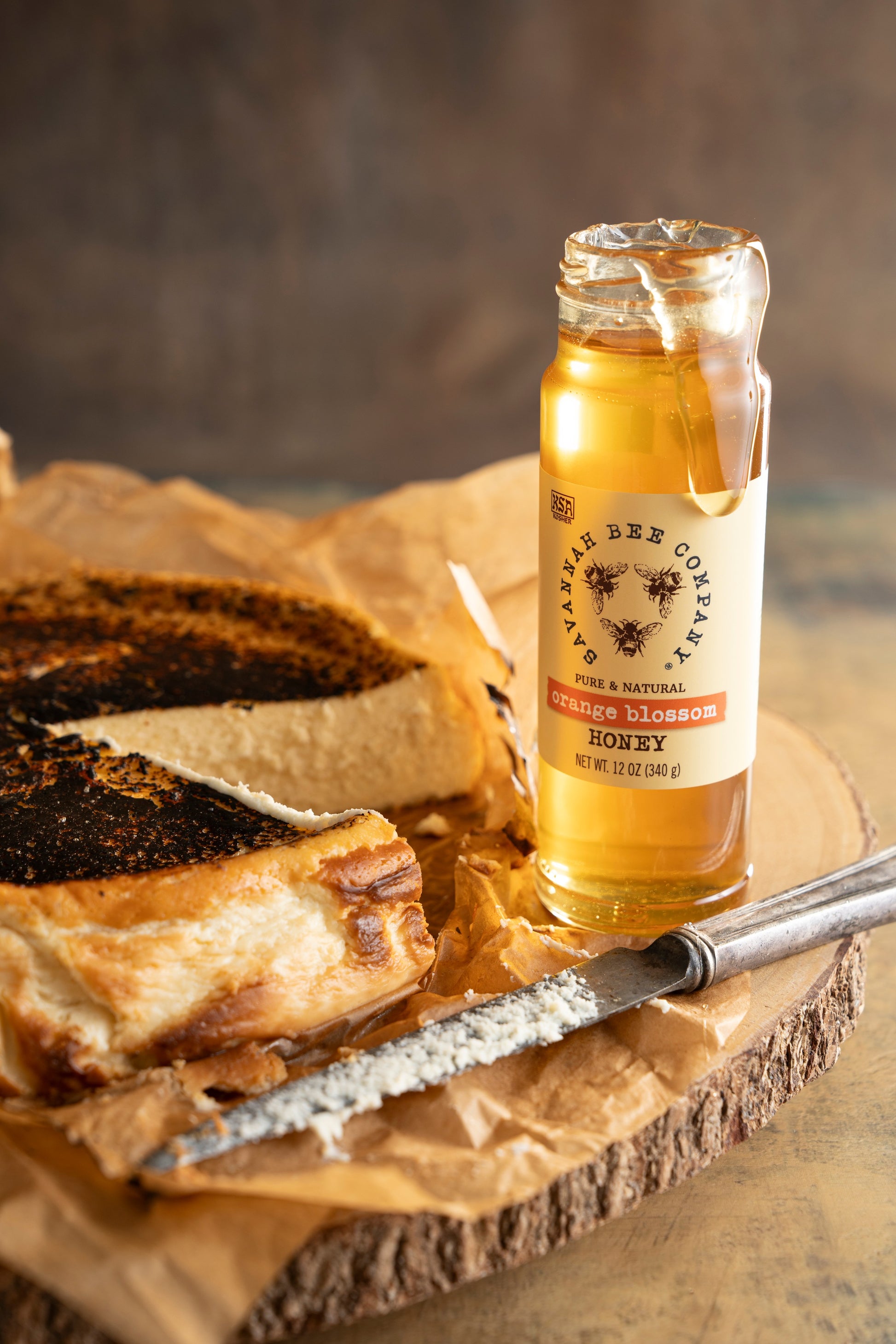 12 ounce orange blossom honey open next to a honey Basque cheesecake on a wooden platter.