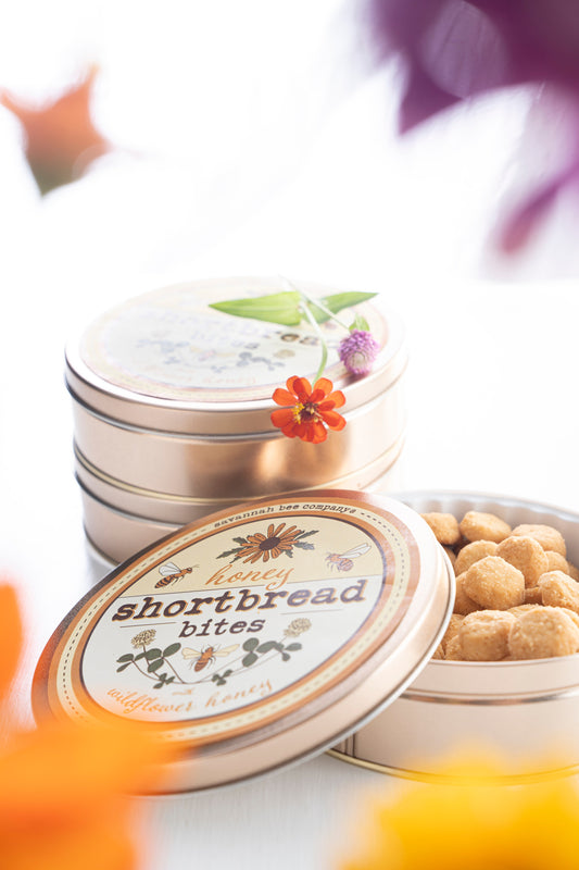Shortbread honey bites in a metal floral tin surround by flowers
