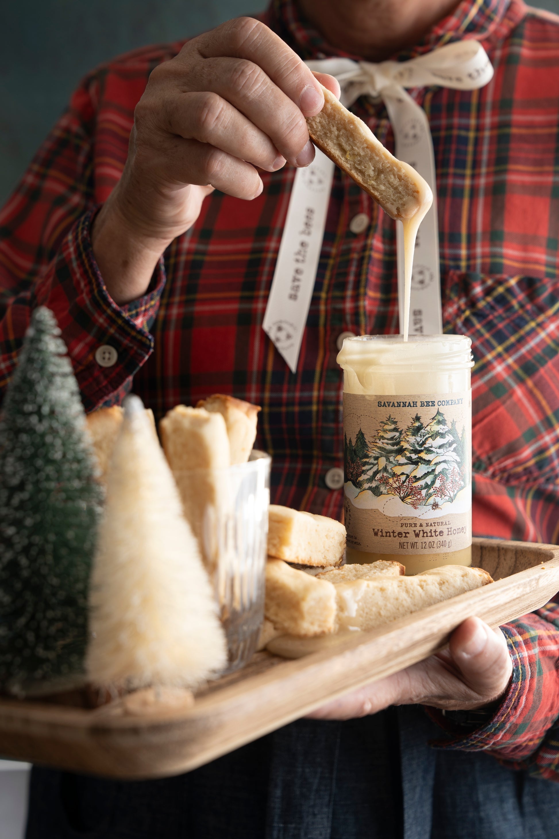 A woman holding a tray of biscuits and dipping one into a 12 ounce jar of winter white honey