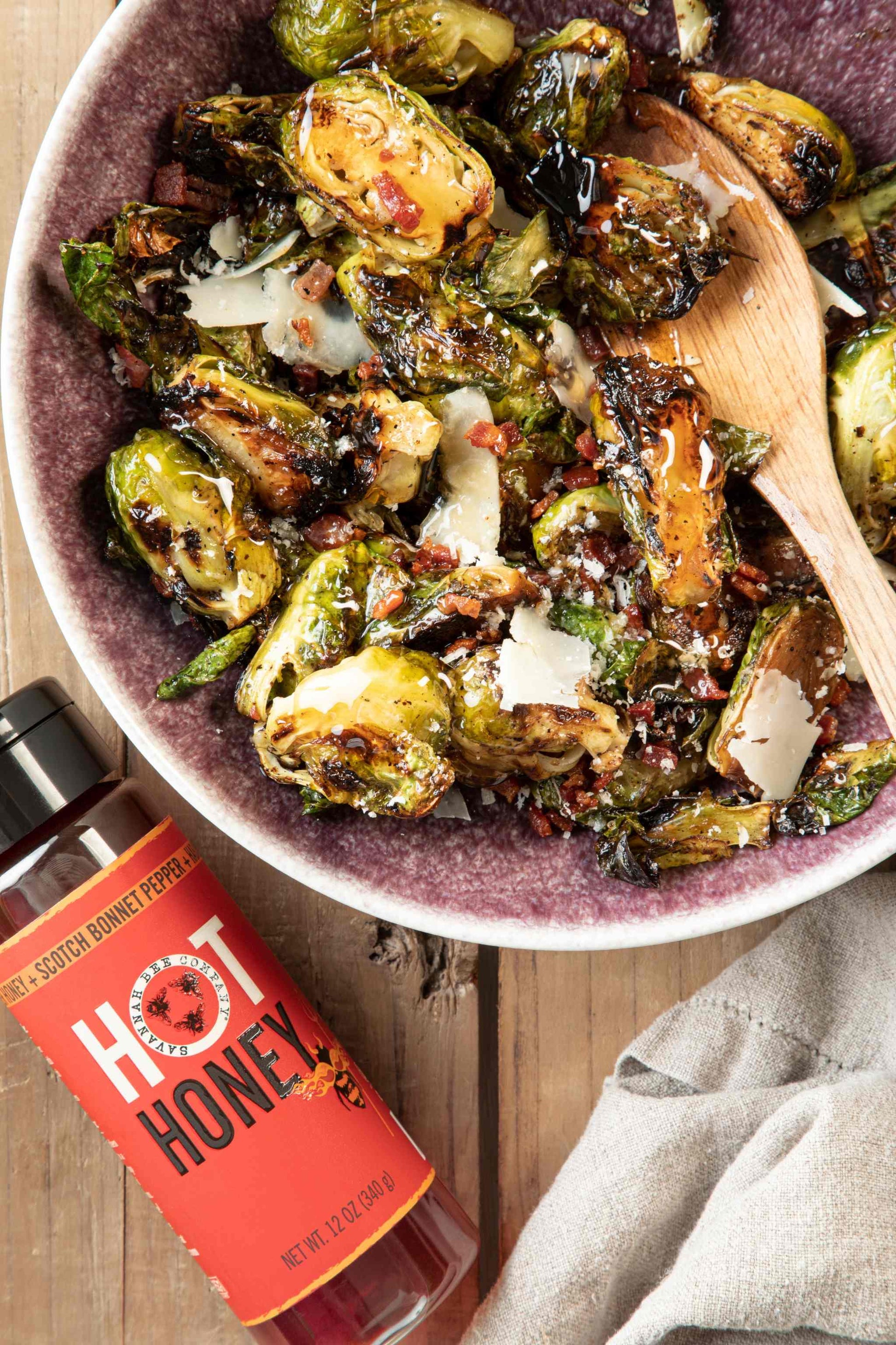 Bowl of hot honey roasted Brussel sprouts next to a 12 ounce hot honey squeeze bottle.